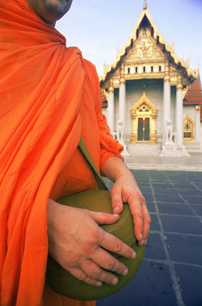 Monk holding alms bowl with temple in the background, Wat Benchamabophit (Marble Temple), Bangkok, Thailand, Southeast Asia, Asia