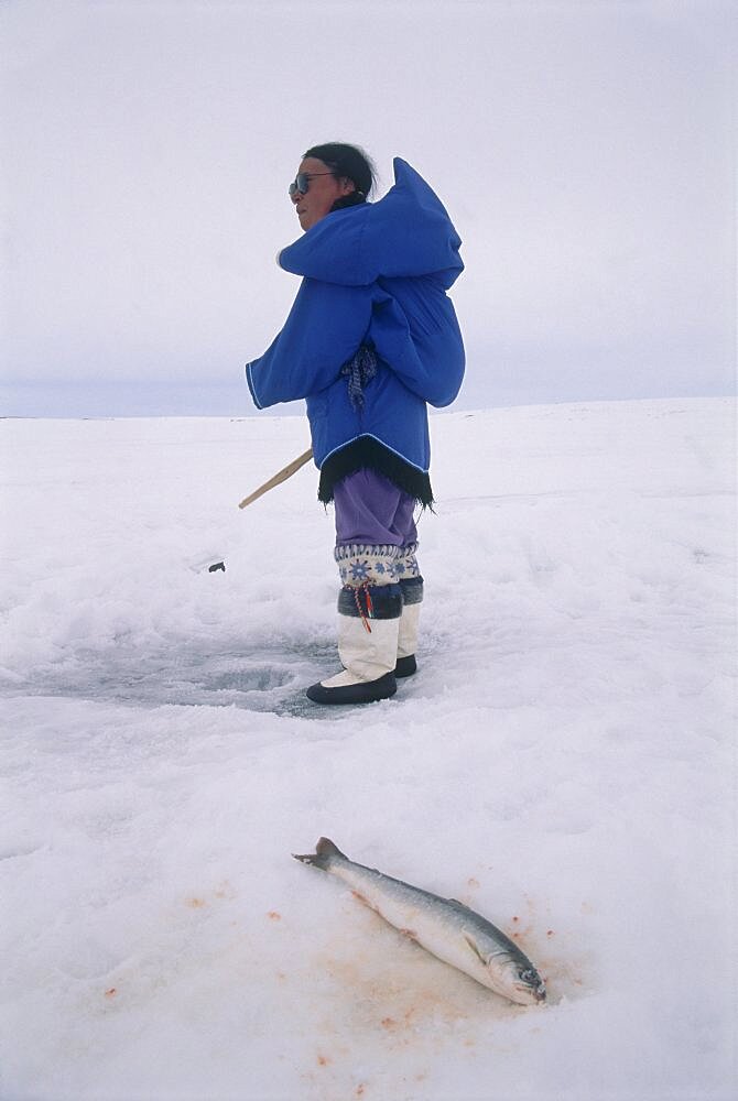 Image of an Eskimo woman ice fishing on a frozen lake in Baffin Canada