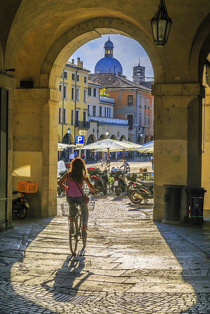 View of cyclist and Piazza delle Erbe through archways and dome of Padua Catherdal visible, Padua, Veneto, Italy, Europe