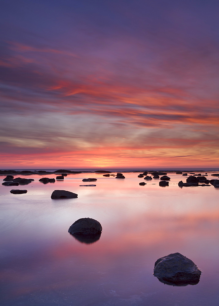 Boulders and reflections in the sea at sunrise, Saltwick Bay, Yorkshire, England, United Kingdom, Europe