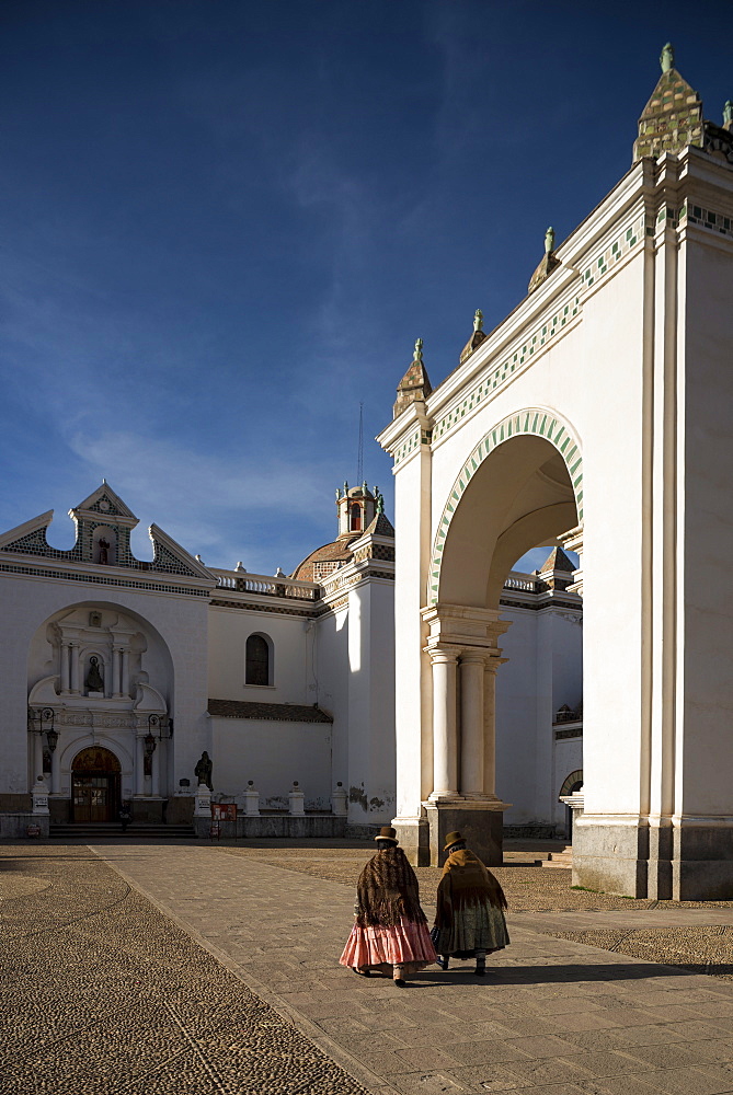 Traditionally dressed women walking past Copacabana Cathedral after dawn, Copacabana, Lake Titicaca, Bolivia, South America