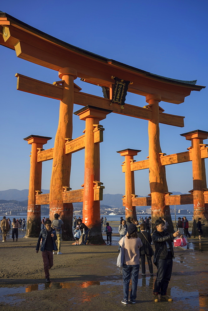 Tourists walking under the torii gate of Miyajima at low tide, Itsukushima, UNESCO World Heritage Site, Hiroshima Prefecture, Honshu, Japan, Asia