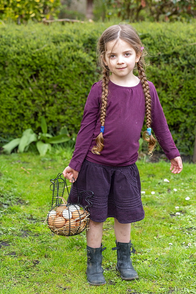 Girl carrying a basket full of chicken eggs in a garden