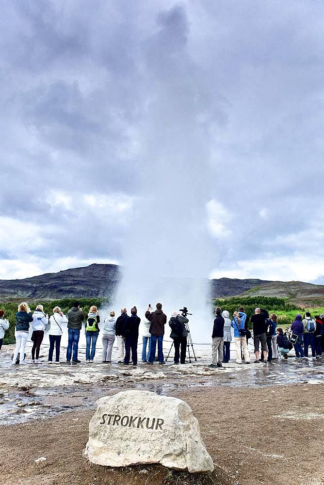 Tourists watching the gushing of a geyser: hot water coming out of the Strokkur geyser, Geysir site, Iceland.