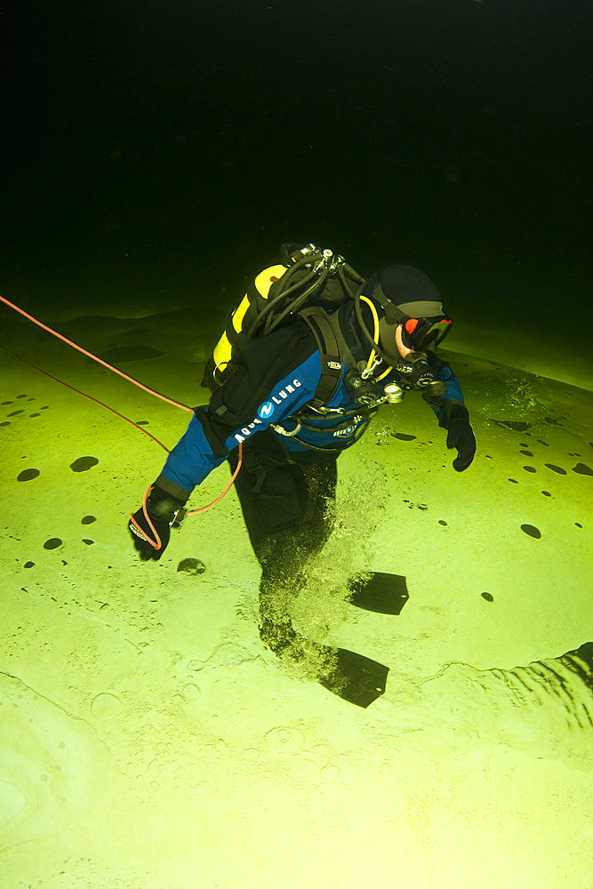 Scuba diver under ice walking upside down, exercise to practice orientation, Arctic circle Dive Center, White Sea, Karelia, northern Russia