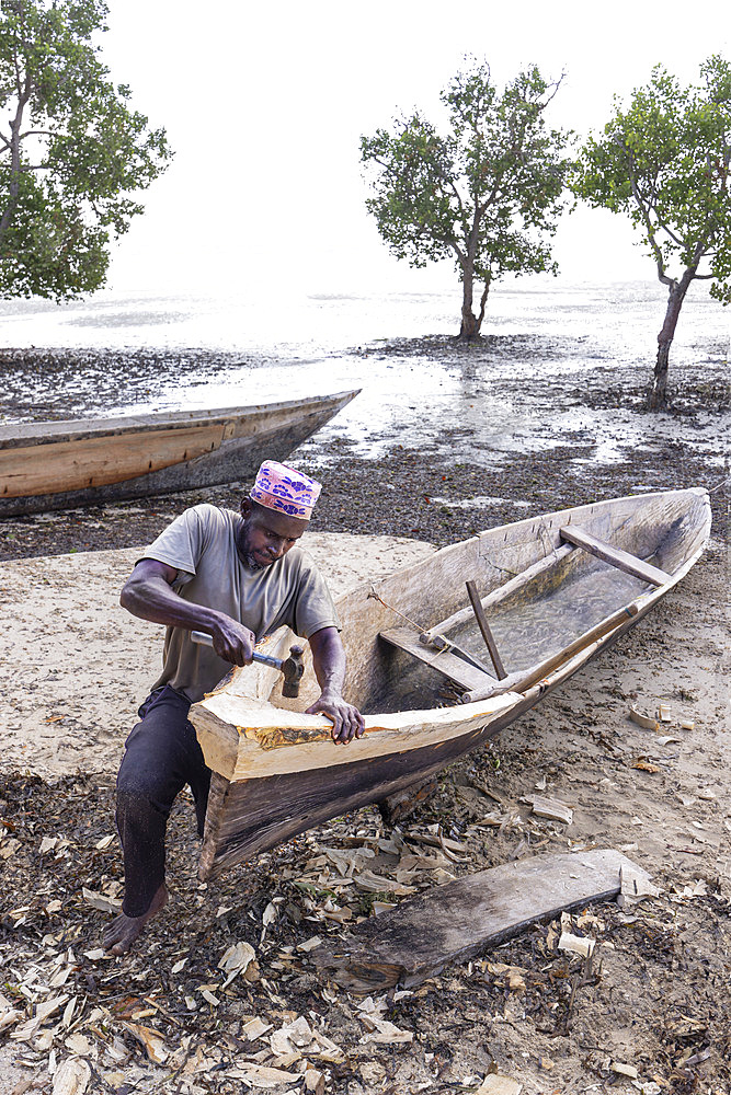 Fisherman repairing his pirogue on a beach at low tide on the east coast of Zanzibar, Tanzania