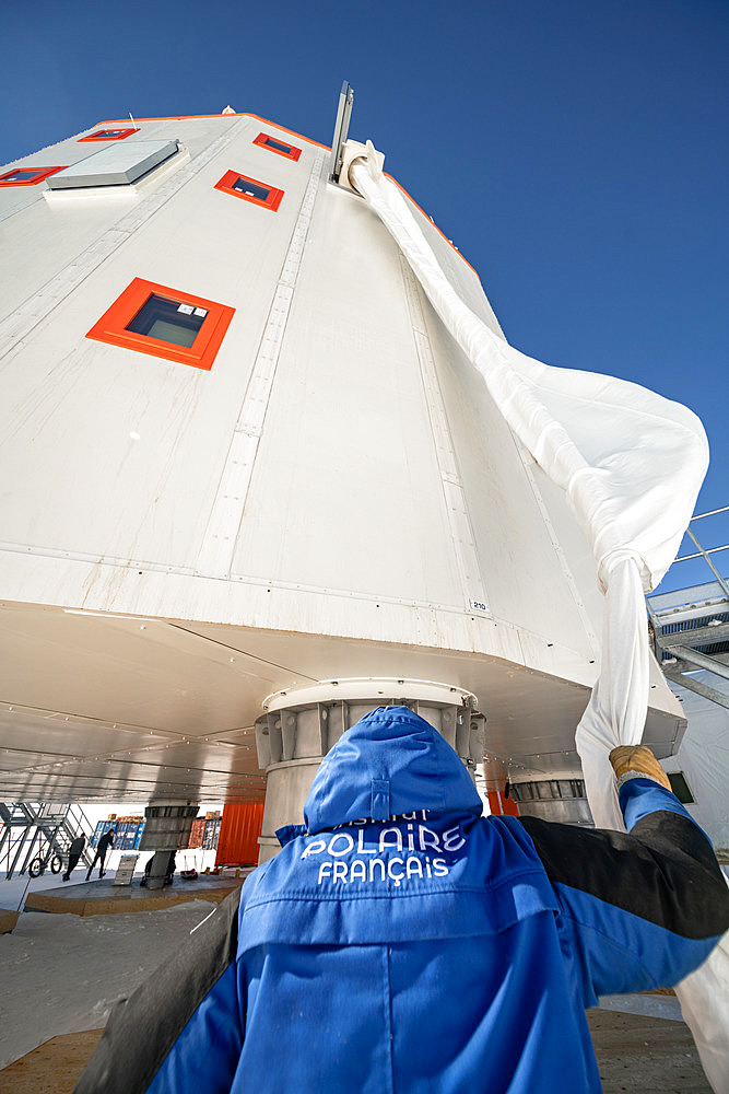 A technician at the foot of the station holds a large evacuation sock into which a person is lowered. Once a month, all the staff carry out an emergency evacuation of the station using a ?sock?. The idea is to let yourself slide down a tube of fabric that slows your fall to such an extent that you can even stop yourself by spreading your arms and legs. A technician is waiting for us at the bottom to assist with the last metre of the descent. Concordia Antarctic Research Station, Dome C plateau, East Antarctica.