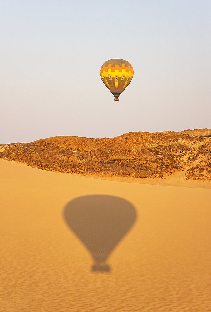 The hot-air balloon above an arid plain and isolated mountain ridges at the edge of the Namib Desert. The shadow is from a second balloon. Aerial view. Namibia.