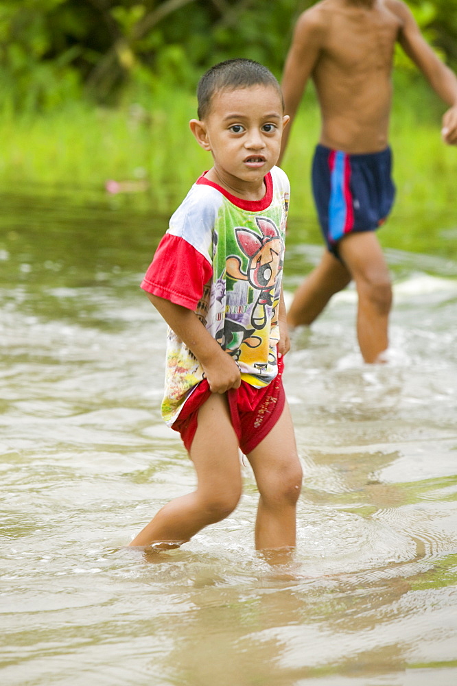 Boy wading through the floodwater caused by sea water incursion due to global warming induced sea level rise that threatens the future of these low lying islands, Funafuti Atoll, Tuvalu, Pacific