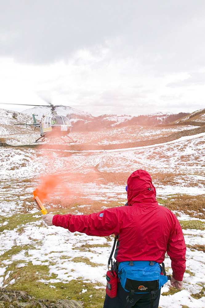 A member of Langdale Ambleside Mountain Rescue Team attracts an air ambulance with a flare to the site of an injured walker on Silver Howe above Grasmere, Lake District, Cumbria, England, United Kingdom, Europe