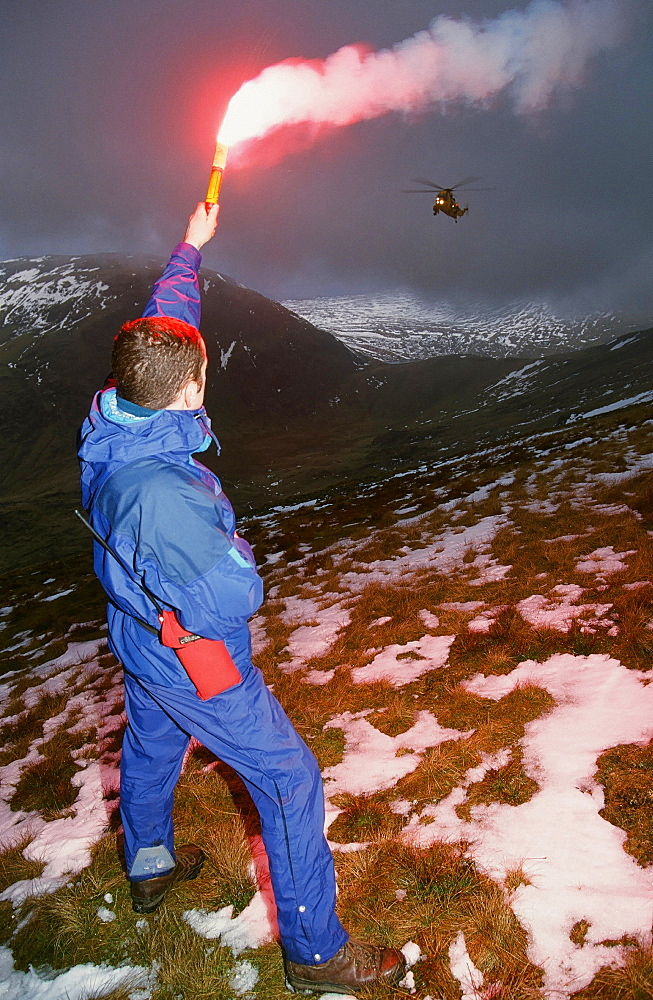 A mountain rescue member uses a flare to attract an approaching Sea King helicopter to the casualty site on Fairfield in the Lake District National Park, Cumbria, England, United Kingdom, Europe