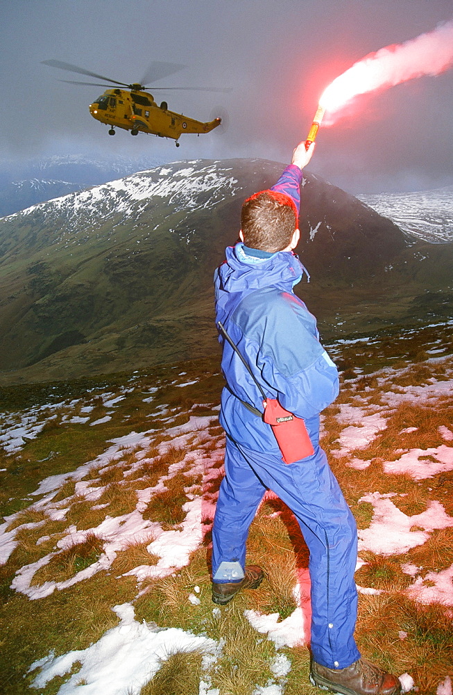 A mountain rescue member uses a flare to attract an approaching Sea King helicopter to the casualty site on Fairfield in the Lake District National Park, Cumbria, England, United Kingdom, Europe