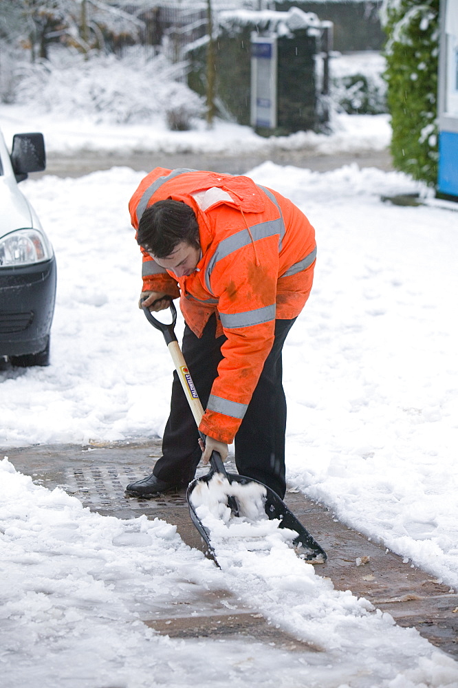 A man shovelling snow at Windermere Train Station, Cumbria, England, United Kingdom, Europe