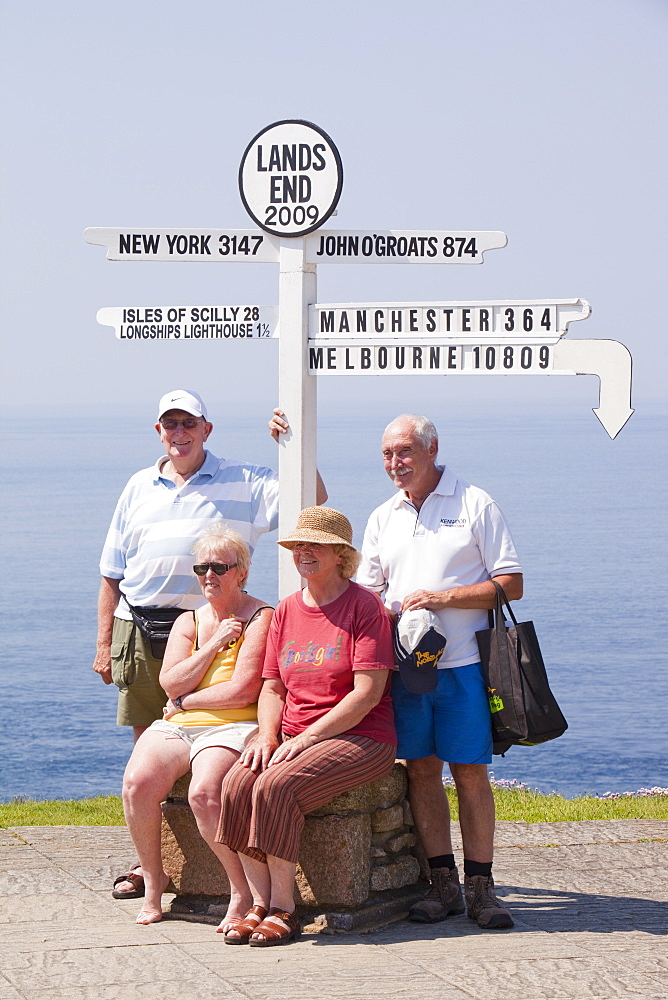 Friends on holiday having their photo taken at Lands End with the distances to the towns where they live, Cornwall, England, United Kingdom, Europe