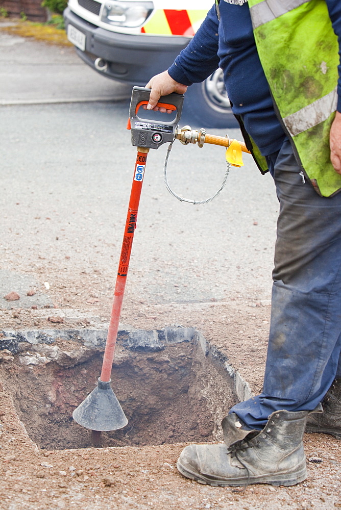 A British Gas worker using a compressed air soil picker to loosen soil around utility pipes as part of a gas pipe replacement upgrade, Cumbria, England, United Kingdom, Europe