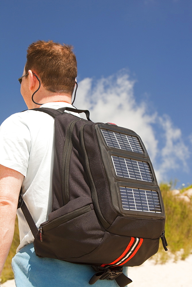 A man carrying a solar backpack, the solar panels can be used for recharging mobile phones and other electrical devices