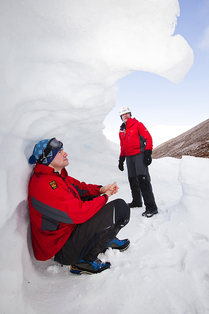 Mountaineers sheltering in an old snow hole in snow banked against an esker in Coire an Sneachda in the Cairngorms, Scotland, United Kingdom, Europe