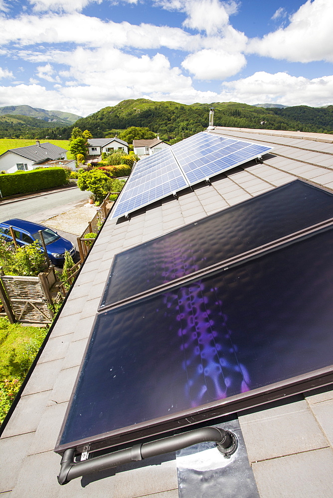 Solar thermal panels for heating hot water with solar PV electric panels behind on a house roof in Ambleside, Lake District, Cumbria, England, United Kingdom, Europe