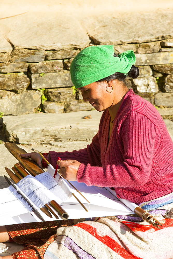 A Nepalese woman in traditional clothing weaving cloth on a hand loom in the Himalayan foothills, Nepal, Asia