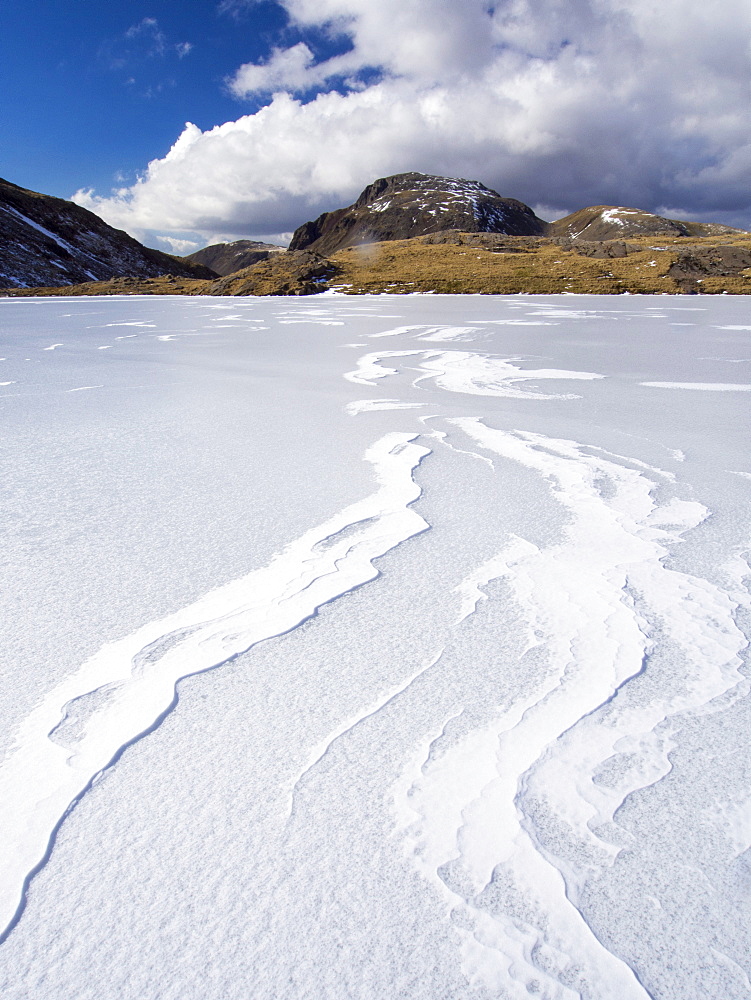 Wind drifted snow on Sprinkling Tarn at the head of  Borrowdale, frozen solid, looking towards Great End, Lake District, Cumbria, England, United Kingdom, Europe