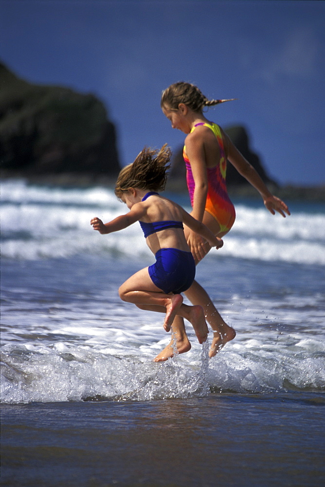 Two young girls jumping over waves, Marloes Sands, Pembrokeshire, Wales, UK, Europe