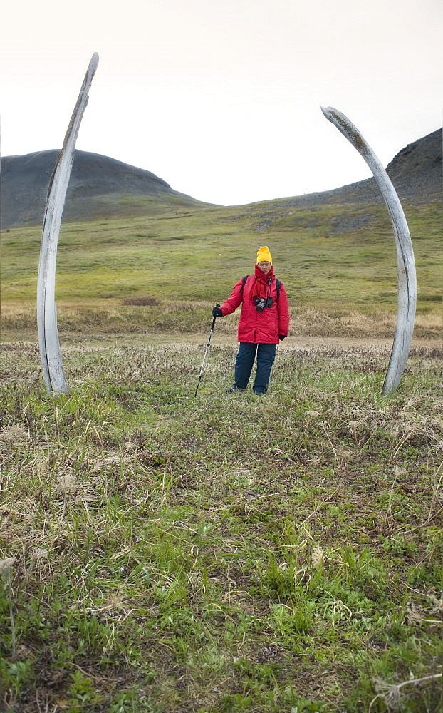 Whalebone Alley, female tourist standing between bow head whale rib bones, Itygran Island (Bering Sea) Russia, Asia.  MORE INFO: Whale Bone Alley was discovered by Soviet archaeologists in 1976, but has remained untouched since and little is known of this place. There is a long double line of bowhead whale bones -- jaws and ribs -- running parallel along the shore for hundreds of yards. Many of the bones, especially the enormous jaw bones, are still standing, propped up by lichen-covered rocks. The location is thought to have been used in about 1300 as a ceremonial site, for a men's secret society or feasting site.