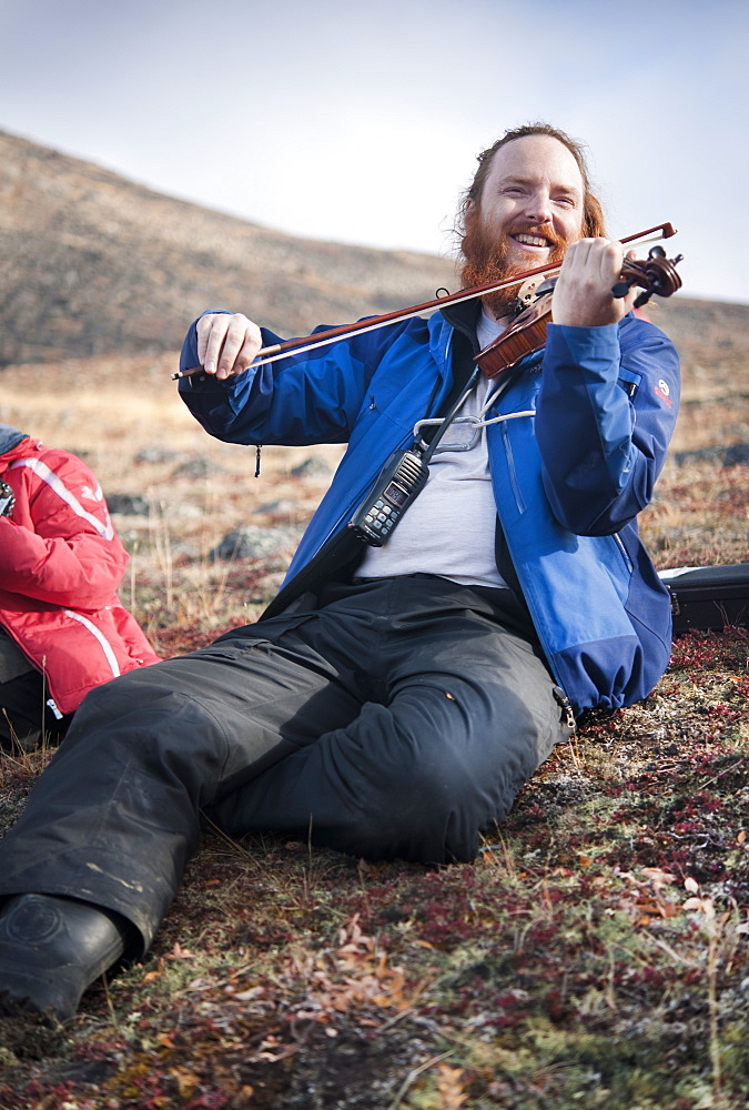 Musician Daniel Payne playing fiddle on mountain side. Pangnirtung, Cape Dyer, Baffin Island, Canada, North America