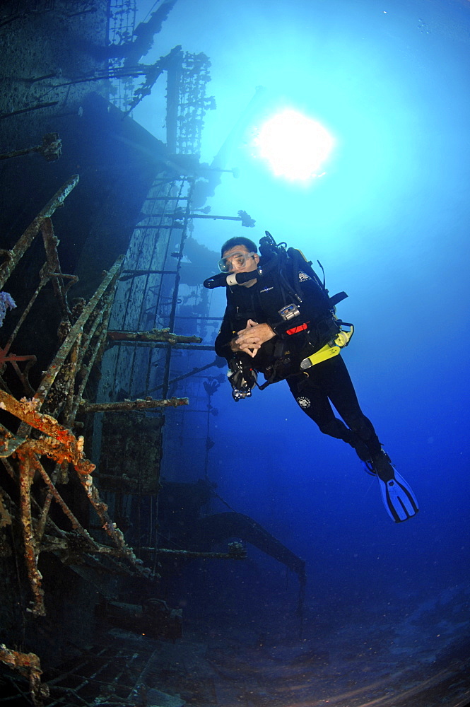 Mixed gas rebreather divers by ship wreck, sunburst on surface behind.  Red Sea.