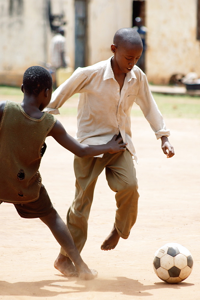 Two African boys committed to the tackle, playing football in the school yard.  Gulu Town, Northern Uganda. . Gulu Town, Uganda, East Africa