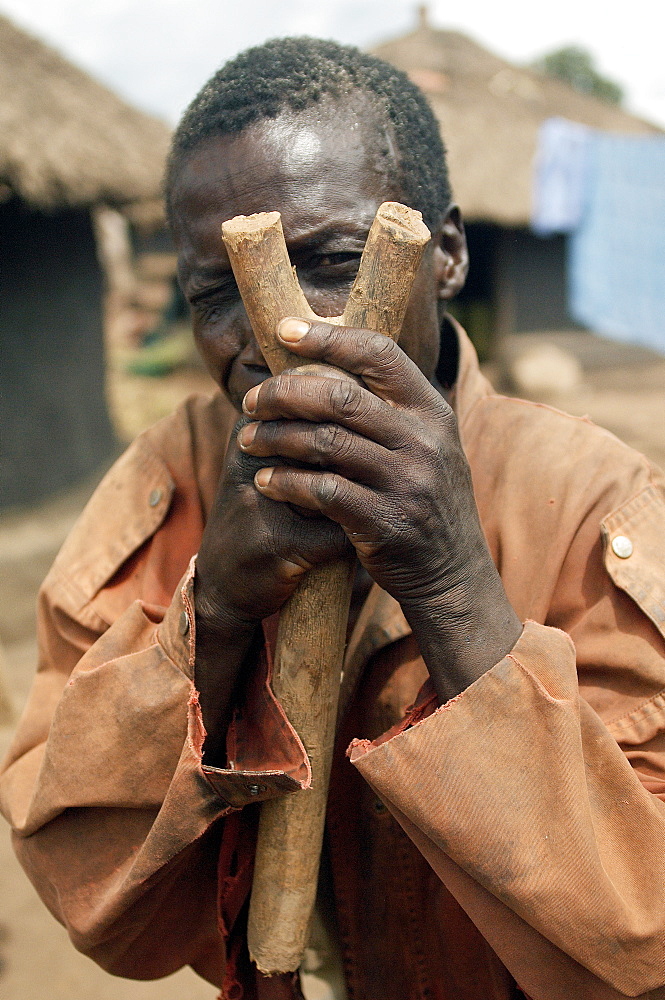 An IDP camp (internally displaced people) in Amuru district of Northern Uganda has been created to accommodate the mass of Ugandan refugees fleeing the LRA (Lords Resistance Army) who are fighting the Ugandan government and its people.  Having fun with the children, this man is mocking my actions with a stick.  With a little imagination, you can see this stick is a camera...!. Amuru, Uganda, East Africa