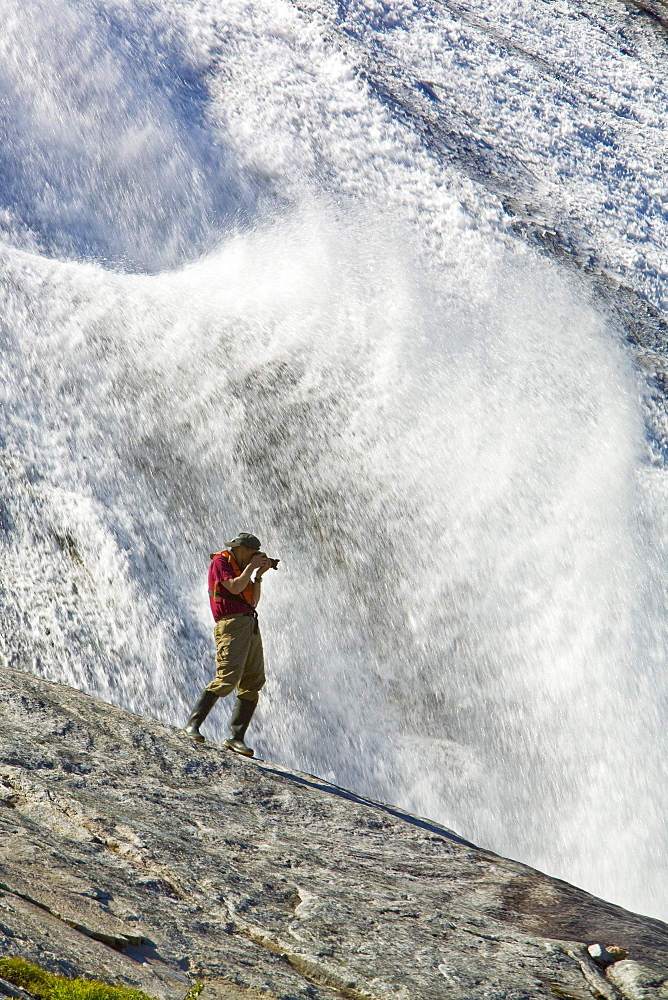 A photographer at a snow melt waterfall in Nordfjord, an arm of the larger Melfjord - situated just above the Arctic Circle - in northern Norway, Barents Sea.