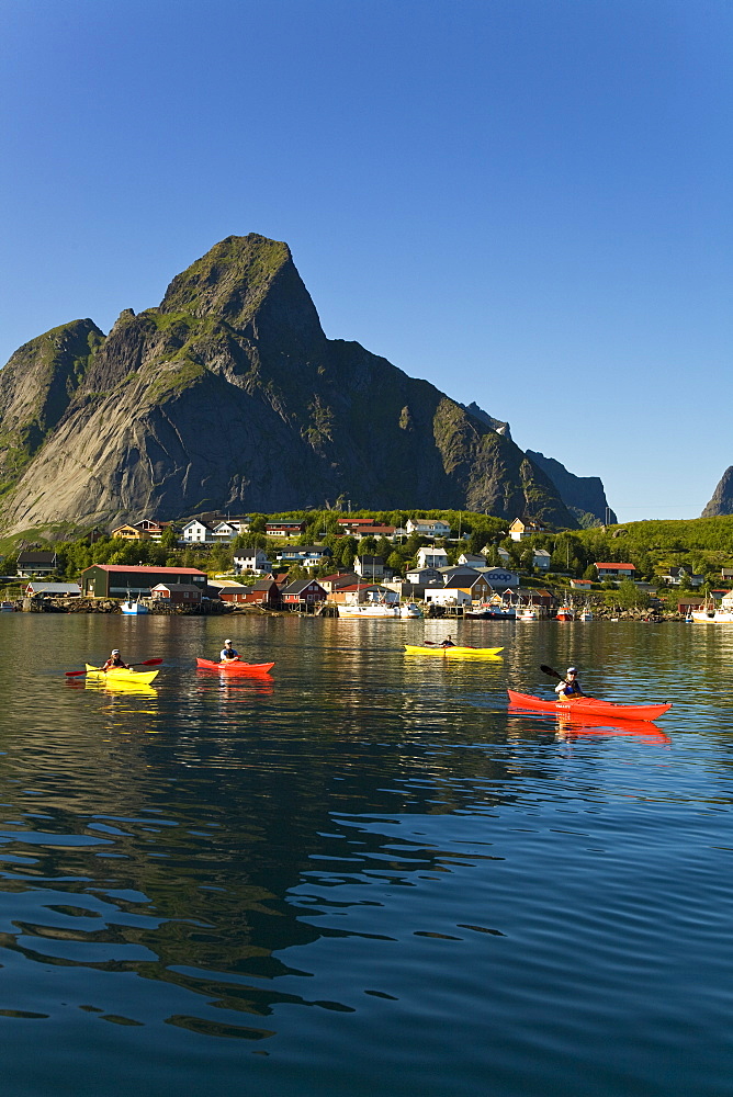 Kayakers in the late evening light on the picturesque Norwegian fishing town of Reine in the Lofoton Island Group, Norway. No model or property releases.