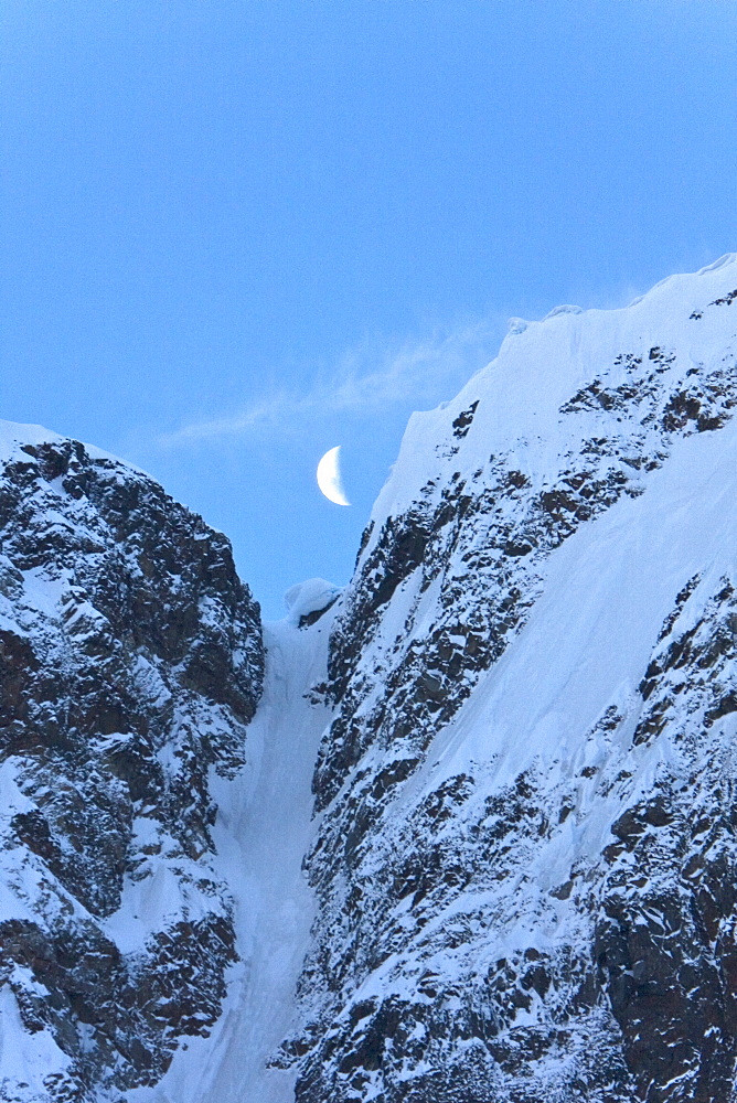 A quarter moon setting over the scenic Lemaire Channel on the west side of the Antarctic peninsula in Antarctica.