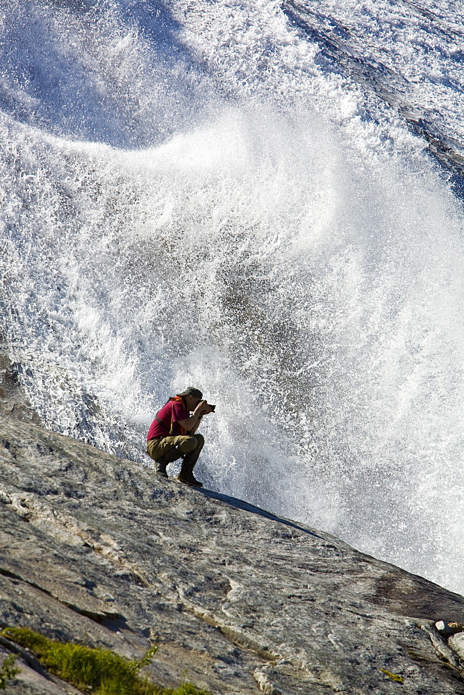 A photographer at a snow melt waterfall in Nordfjord, an arm of the larger Melfjord - situated just above the Arctic Circle - in northern Norway, Barents Sea.