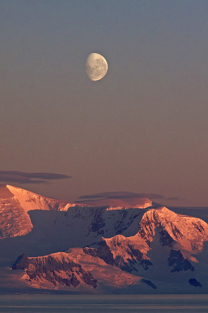 The Lindblad Expedition ship National Geographic Explorer in Dahlman Bay in late evening light as the waxing moon rises on the west side of the Antarctic Peninsula in Antarctica. 