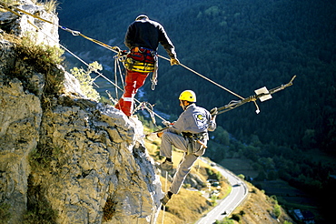 Working high above the busy road below, the two workers first secure the loose boulder to the cliff with a long metal pole.