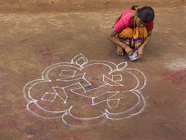 A woman performs the morning ritual of making a Rangoli, a Hindu religious decoration, outside her home in Hampi, Karnataka, India