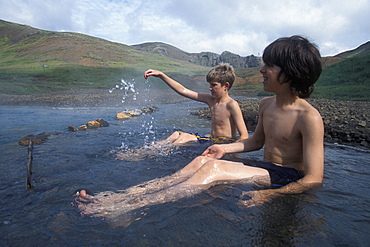 An American boy and an Icelandic boy take a dip in a naturally heated stream in the Valley of Steam near Hveragerdi, Iceland