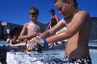 An American boy and an Icelandic boy enjoy the soothing mud of Blue Lagoon near Reykjavik, Iceland