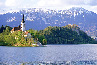 The Church of the Assumption and Bled Castle rise above Lake Bled, Slovenia, with the Kanmik-Savinja Alps rising in the background.