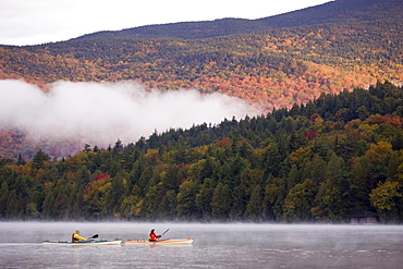 Fit, middle-age couple sea-kayak on Lake Placid in autumn, New York, USA.