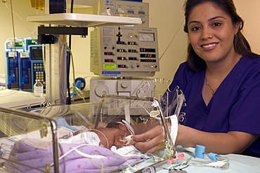 A mother stands next to the incubator in which her premature child rests.