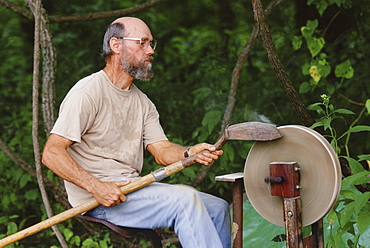 A fieldworker sharpens shovels the old fashioned way at the Big Eddy, an Archaeological site on the Sac River in southwestern, MO.  Archaeologist Neal Lopinot from Missouri State University has been digging their since 1997 to gain a more complete understanding of the prehistoric record in North America.  (Photo by David McLain, Aurora)