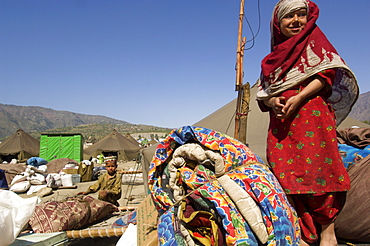 A girl in the Meira tent camp for earthquake survivors stands on top of a pile of her family's belongings as they wait for transportation from the camp, where they have spent the winter, back to their devastated mountain village, in the NWFP, Pakistan.  The Pakistani army, which runs the camp, has mandated that the camps be cleared by early April, despite the fact that many families are afraid or unprepared to return to their devastated homes. The Meira Tent camp (also called Mera, or Maria camp), is located on the Indus River in the Battagram district.  The camp, the largest for displaced people in Pakistan, hosts over 21,000 earthquake survivors, primarily from the Allai valley in Pakistan's NWFP, one of the areas worst-hit by the October 8, 2005 earthquake.