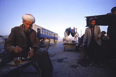 An Afghan man sits on his wooden cart and drinks tea at dawn from a street tea stall in central Kabul.    With the first  respite from war in nearly two decades, Kabulis are busy re-building their lives and business amongst the ruins, and the streets are busy with markets, tea stalls, trucks, etc.  Much of Kabul  was  destroyed in the mid 1990's (1992-1996) in factional fighting between rival mujahideen commanders for control of the capital after the Soviet's withdrawal.