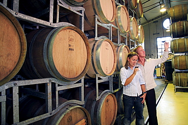 Young couple in their late 20's taste wines in the wine cellar at West Brook Wines in Kumeu, West Auckland, while looking at the stacks of barrels of ageing wines.