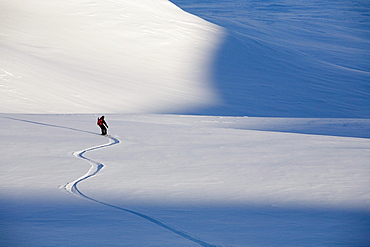 Man snowboards down gentle slope in late afternoon.