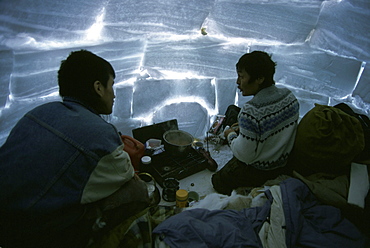 Two men inside an igloo while on a polar bear hunt.