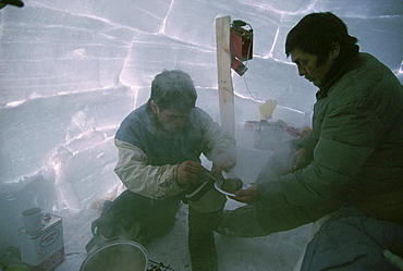 Two men inside an igloo while on a polar bear hunt.