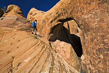 A man hiking next to a sandstone arch, Moab, Utah.